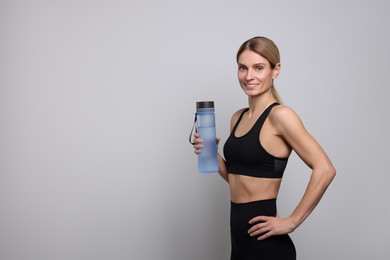 Sportswoman with bottle of water on light grey background, space for text