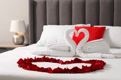 Photo of Honeymoon. Swans made with towels and heart of beautiful rose petals on bed in room