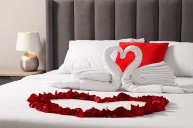 Honeymoon. Swans made with towels and heart of beautiful rose petals on bed in room