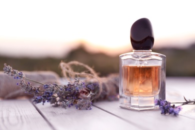 Bottle of luxury perfume and lavender flowers on white wooden table outdoors. Space for text