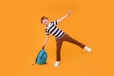 Happy schoolboy with backpack on orange background