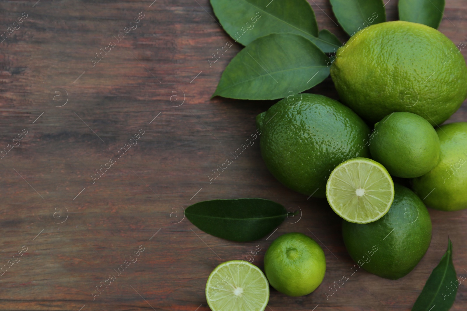 Photo of Whole and cut fresh ripe limes with green leaves on wooden table, flat lay. Space for text