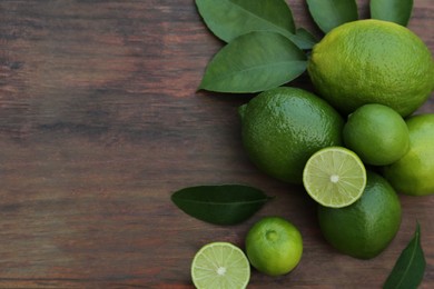 Photo of Whole and cut fresh ripe limes with green leaves on wooden table, flat lay. Space for text