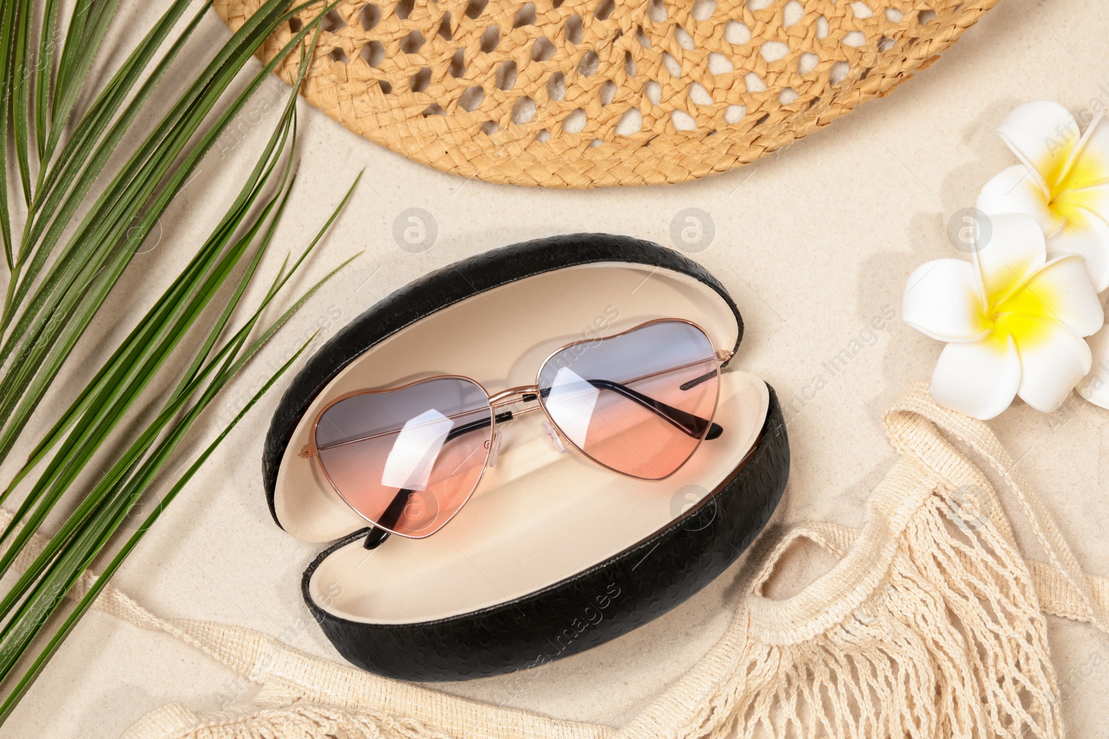 Photo of Flat lay composition with stylish sunglasses in black leather case on sand