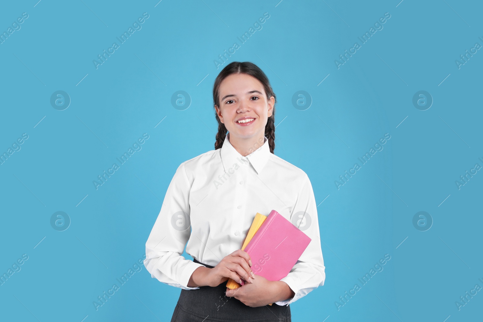 Photo of Teenage girl in school uniform with books on light blue background