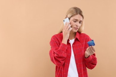 Photo of Stressed woman with credit card talking on smartphone against beige background, space for text. Be careful - fraud