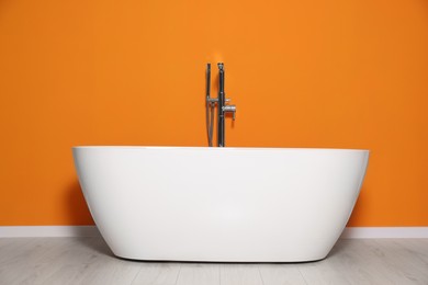 Stylish ceramic tub in near orange wall indoors