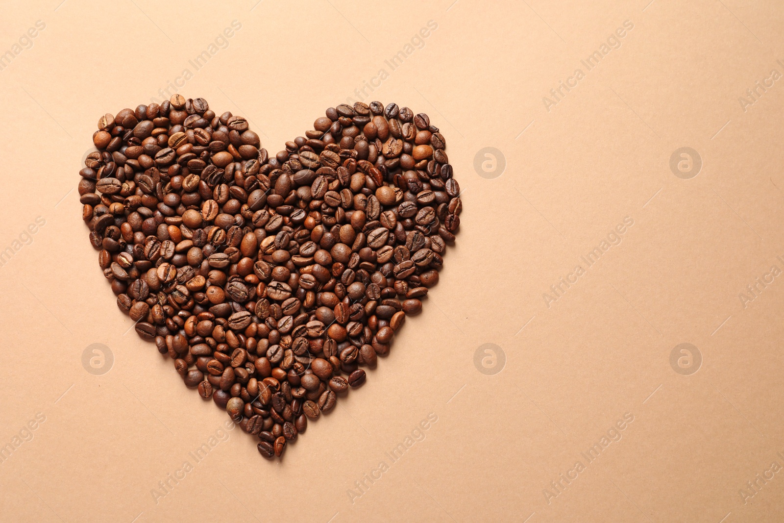 Photo of Heart shaped pile of coffee beans on light orange background, top view with space for text