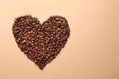 Heart shaped pile of coffee beans on light orange background, top view with space for text