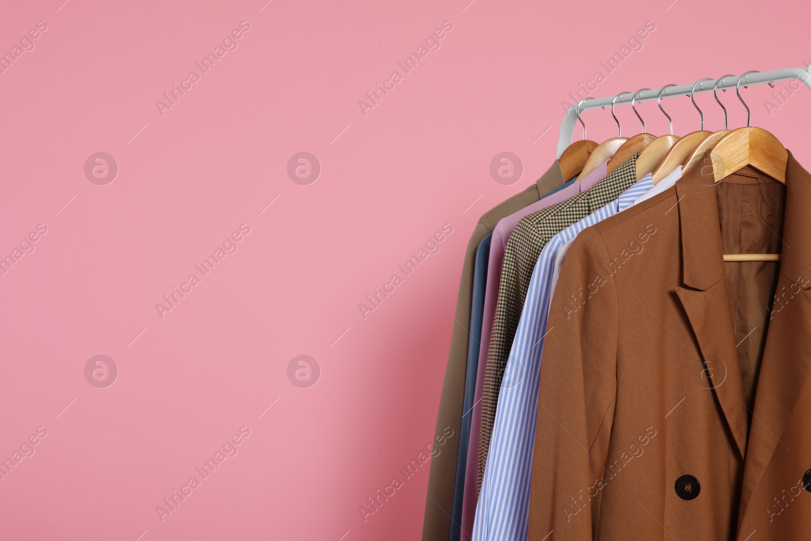 Photo of Rack with stylish clothes on wooden hangers against pink background, space for text