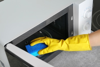 Photo of Woman cleaning microwave oven with sponge in kitchen, closeup