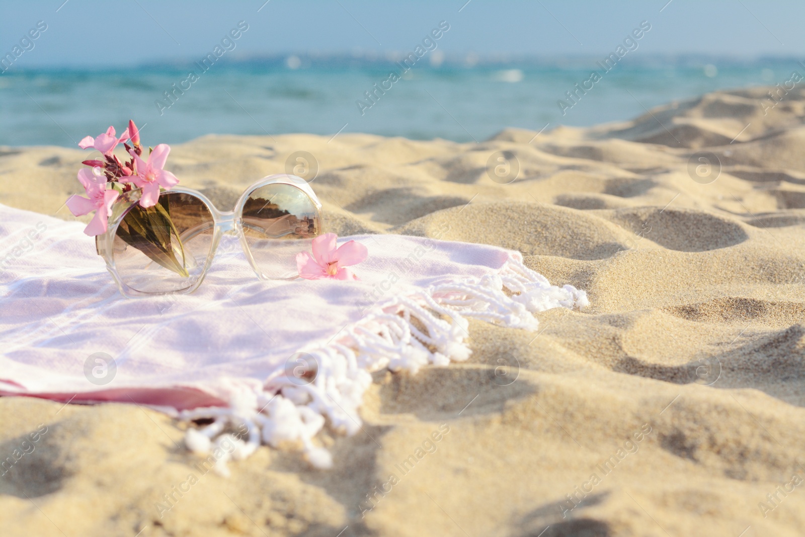 Photo of Beautiful sunglasses with tropical flower on blanket near sea. Space for text