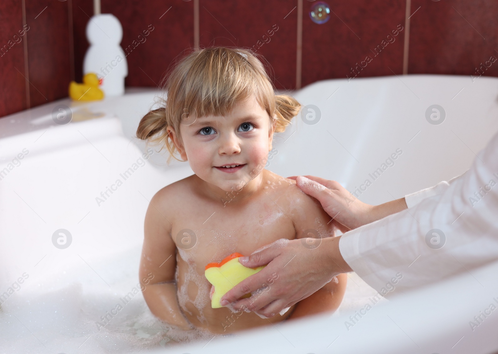 Photo of Mother washing her smiling daughter with sponge in bathtub, closeup