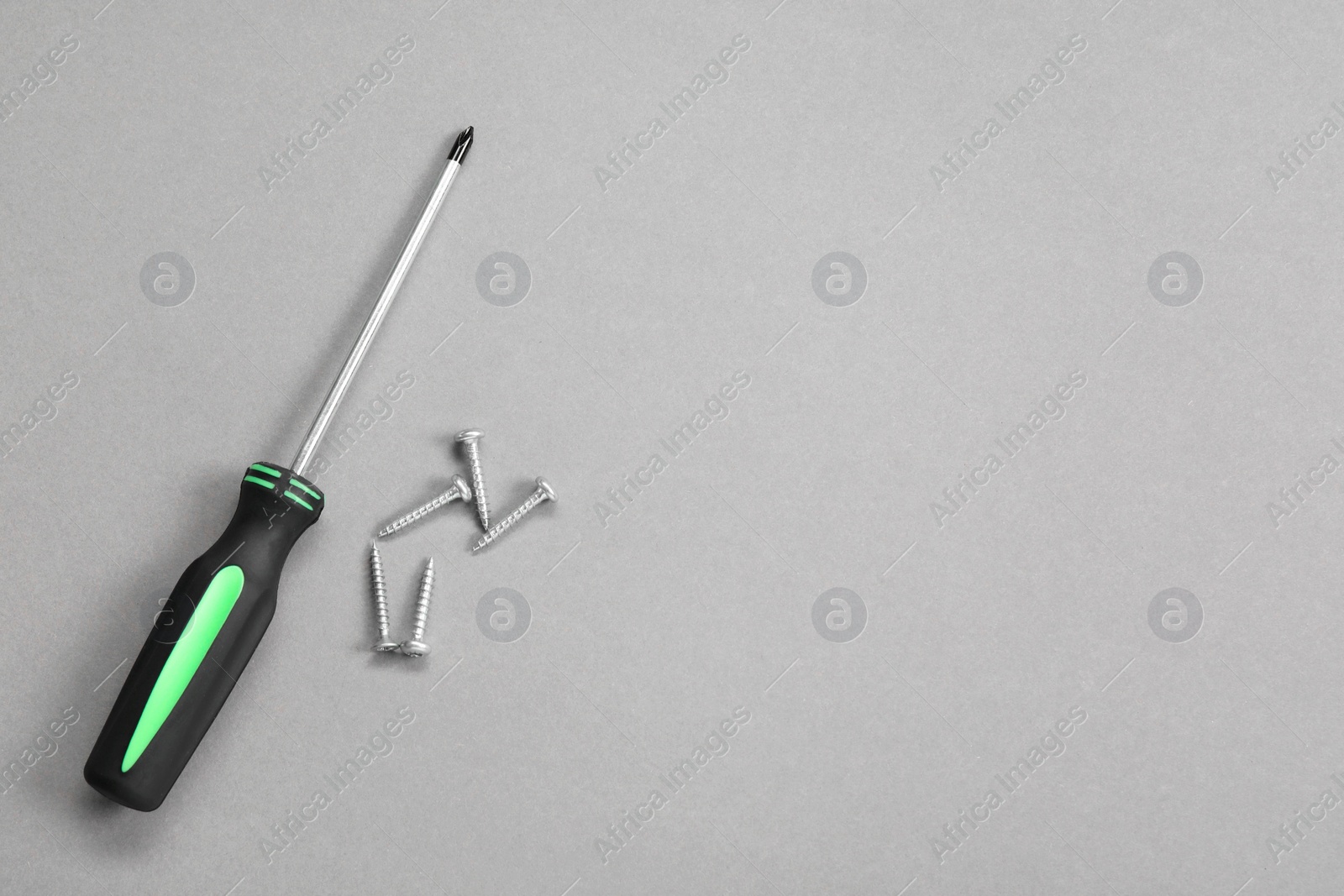 Photo of Screwdriver with black handle and screws on grey background, flat lay. Space for text