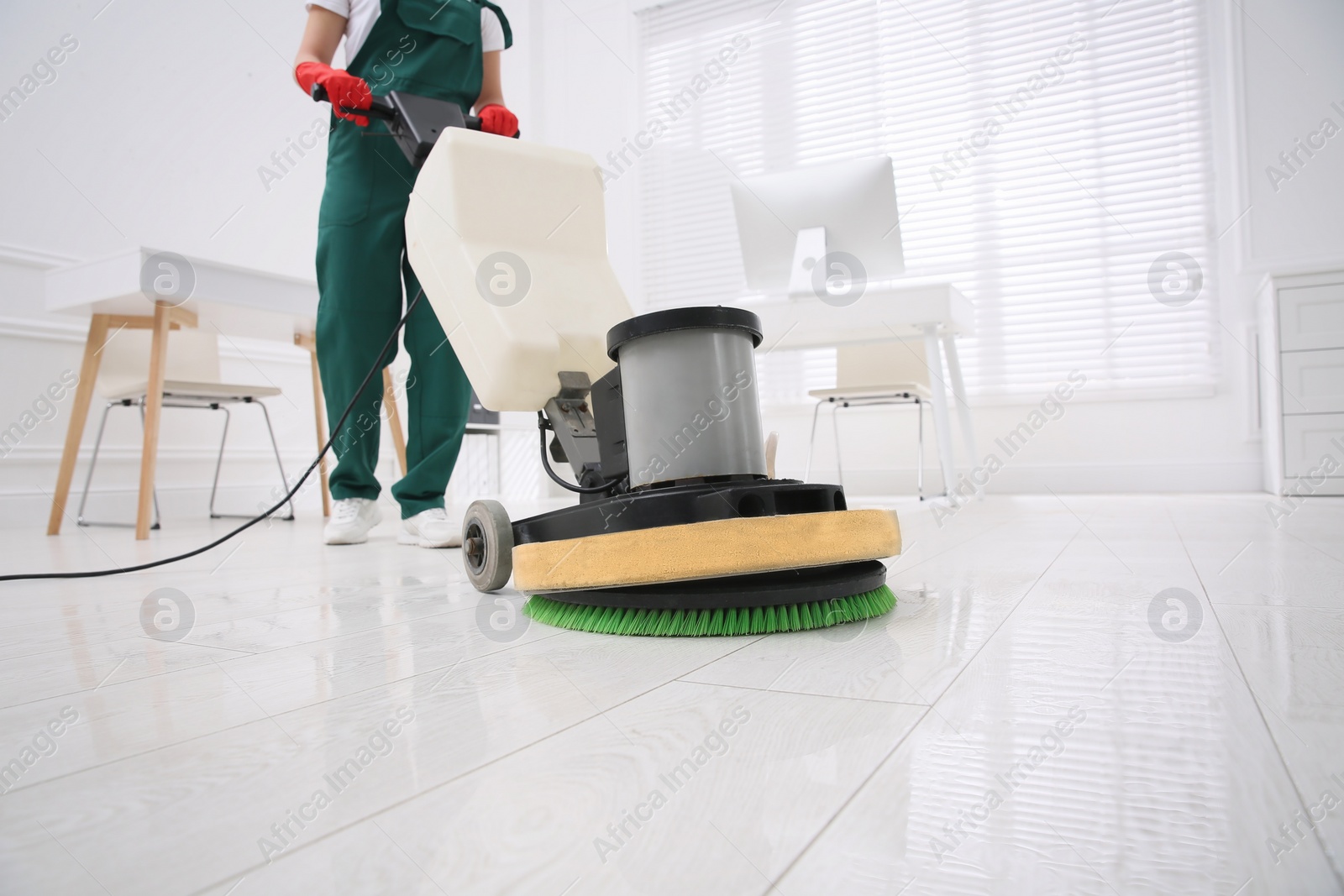 Photo of Professional janitor cleaning parquet floor with polishing machine in office, closeup