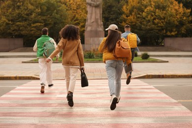 Photo of Being late. Group of students running on pedestrian crossing outdoors, back view