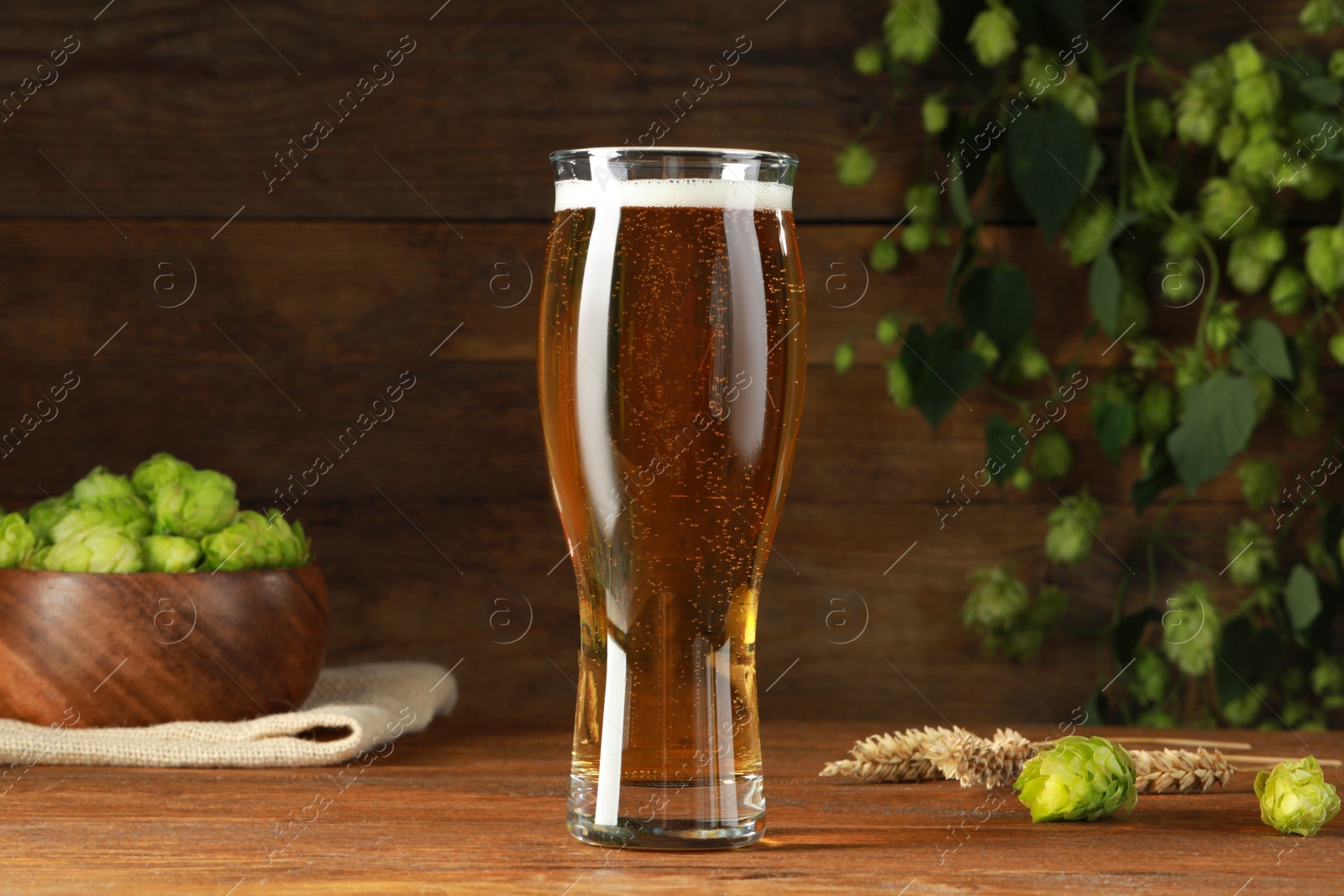 Photo of Glass of beer, fresh green hops and spikes on wooden table