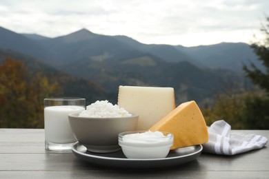 Photo of Tasty cottage cheese and other fresh dairy products on grey wooden table in mountains