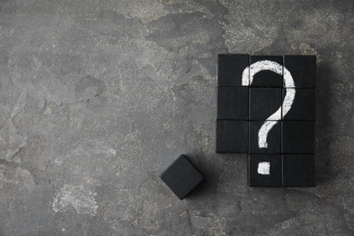Black wooden cubes with question mark on grey stone table, flat lay. Space for text