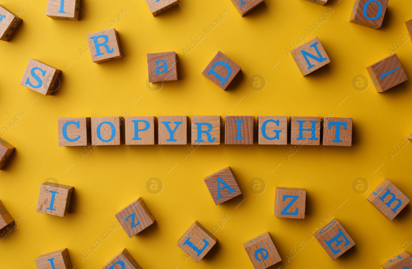 Photo of Plagiarism concept. Word Copyright made of wooden cubes on yellow background, top view