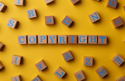 Photo of Plagiarism concept. Word Copyright made of wooden cubes on yellow background, top view