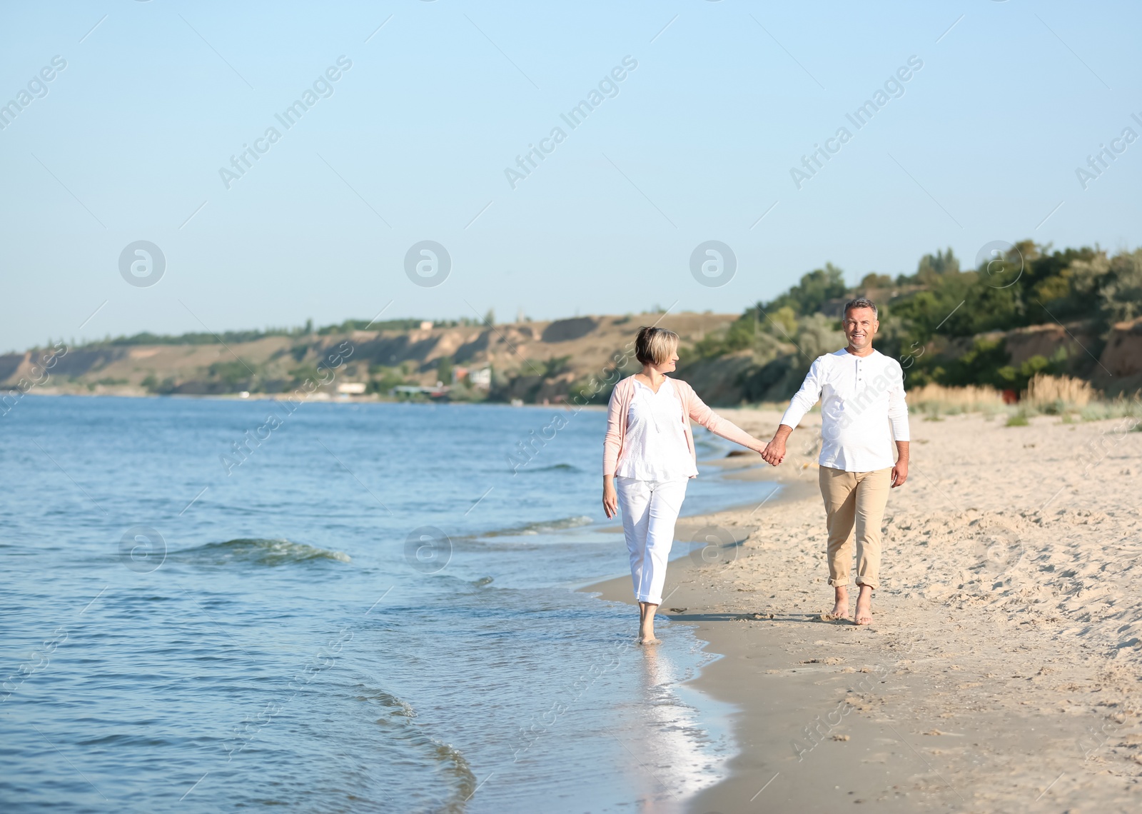 Photo of Happy mature couple walking at beach on sunny day