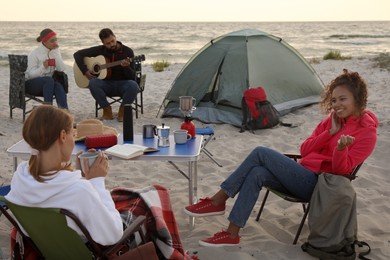 Friends resting near camping tent on sandy beach