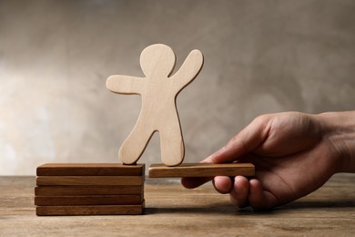 Photo of Woman holding wooden block with human figure at table, closeup