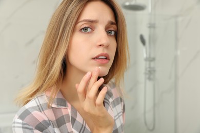 Woman with herpes applying cream onto lip in bathroom