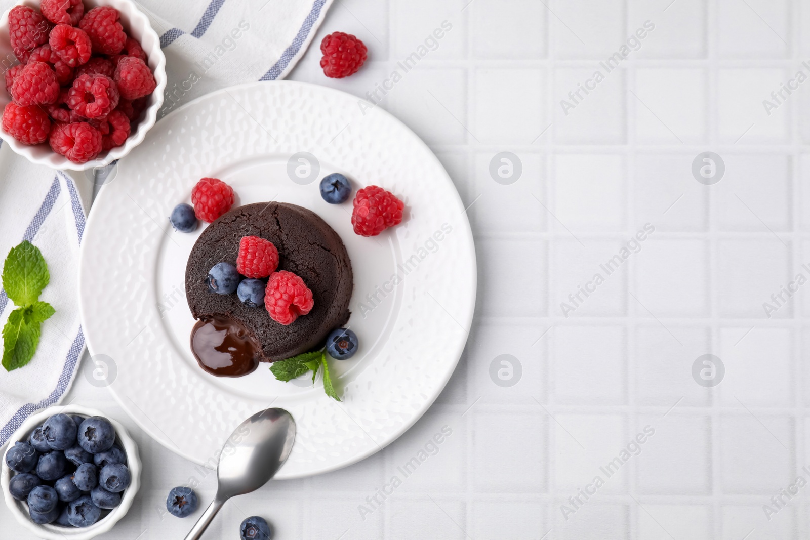 Photo of Plate with delicious chocolate fondant, berries and mint on white tiled table, flat lay. Space for text