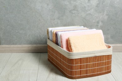 Laundry basket with clean terry towels on floor near grey wall