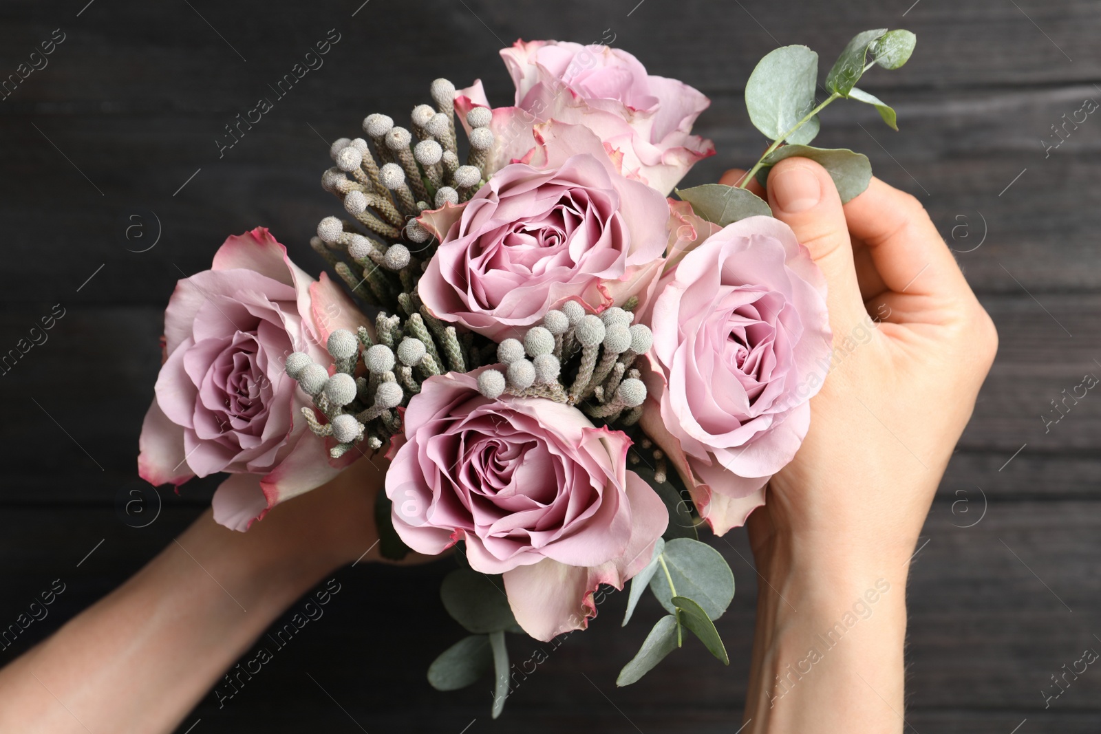 Photo of Florist creating beautiful bouquet at black wooden table, top view