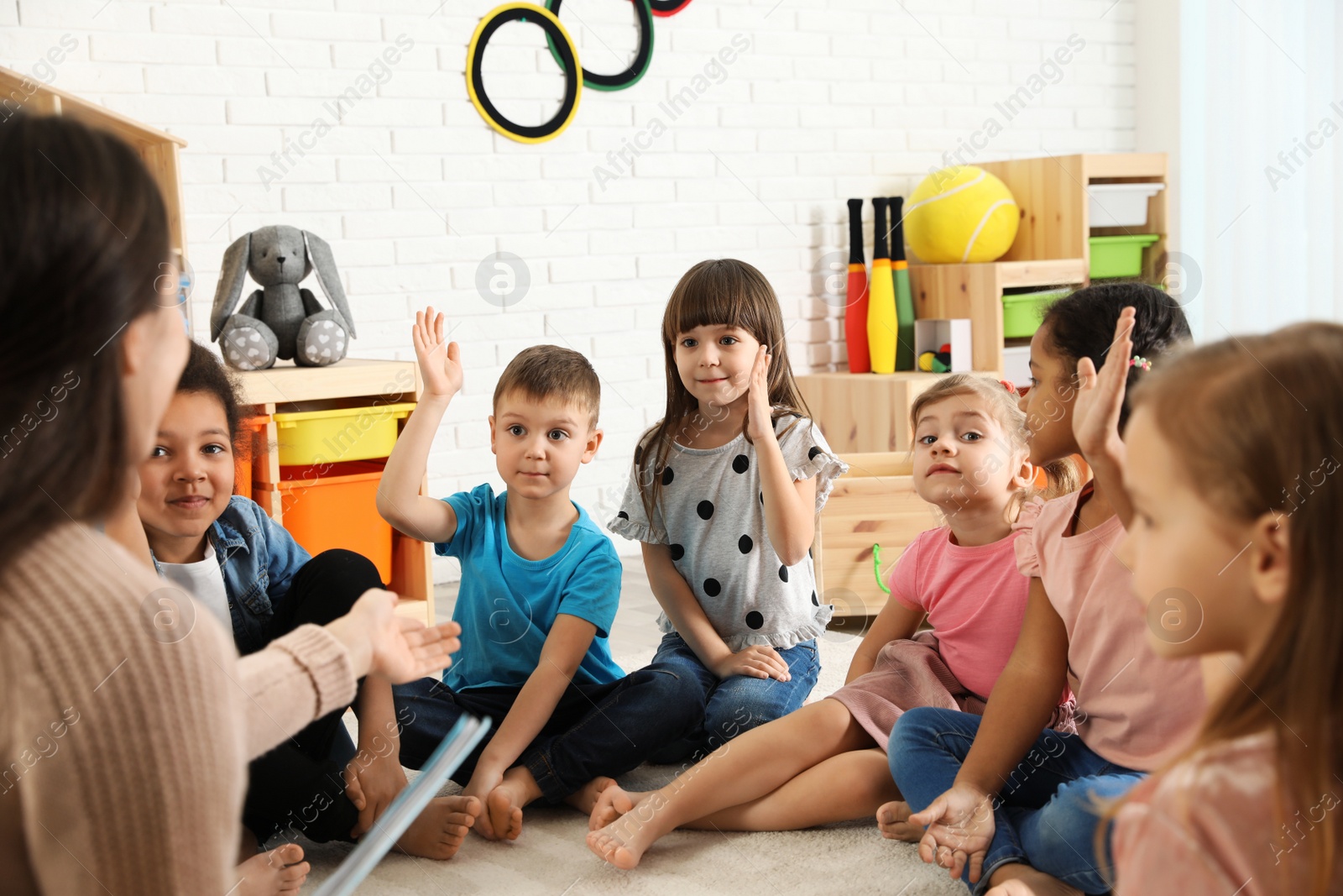 Photo of Kindergarten teacher reading book to cute little children indoors