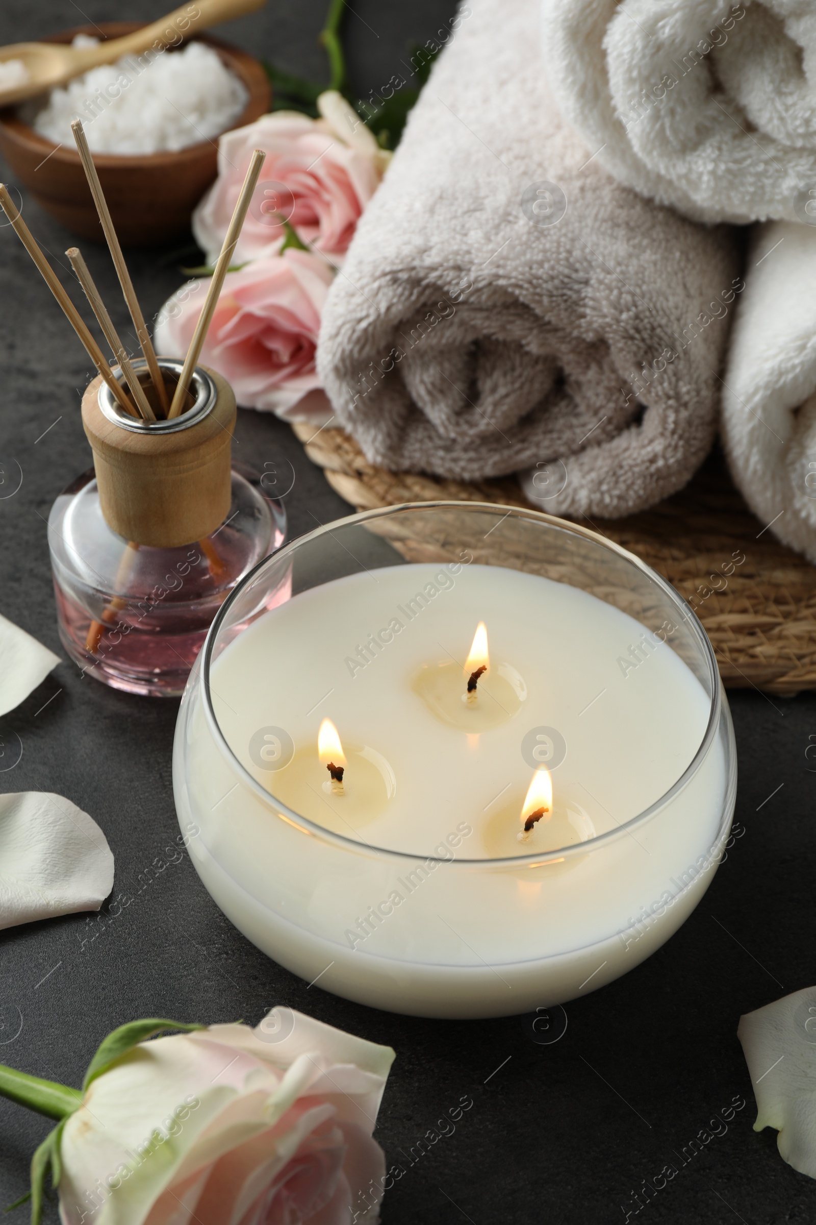 Photo of Spa composition with burning candle and towels on grey table