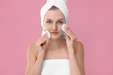 Photo of Young woman cleaning her with cotton pads on pink background