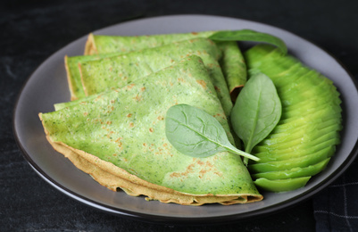 Photo of Delicious spinach crepes with avocado on black table, closeup