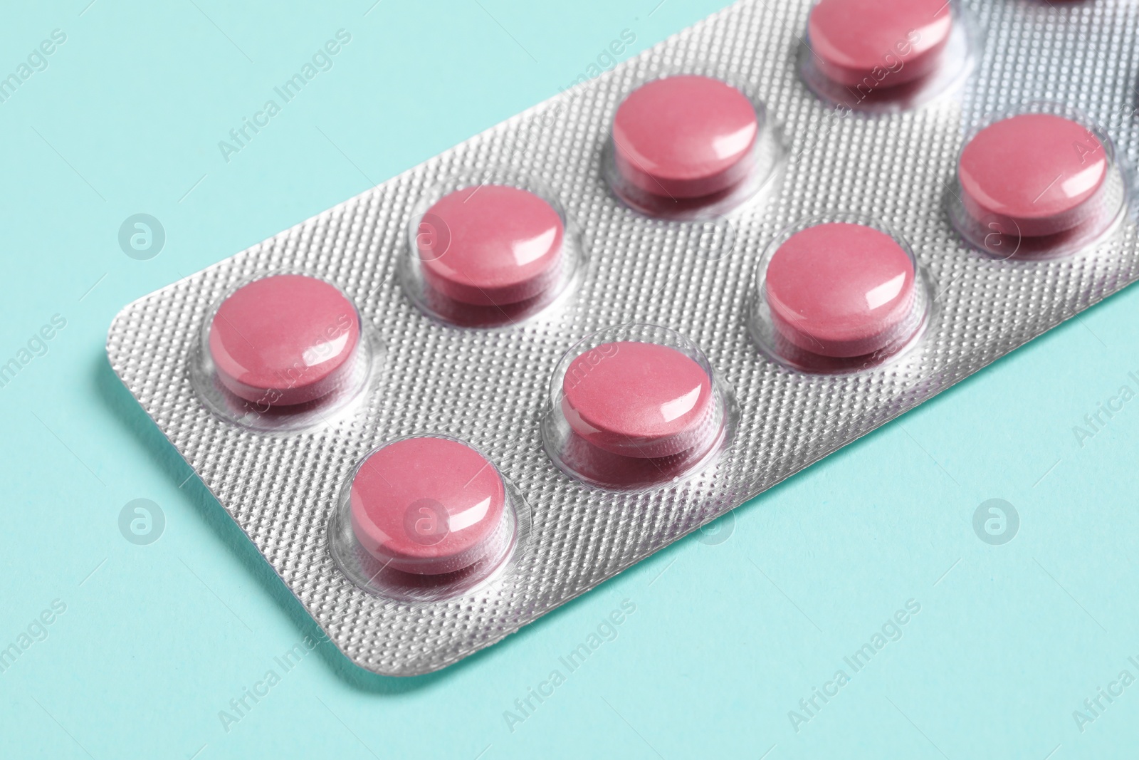 Photo of Pink pills in blister on turquoise background, closeup