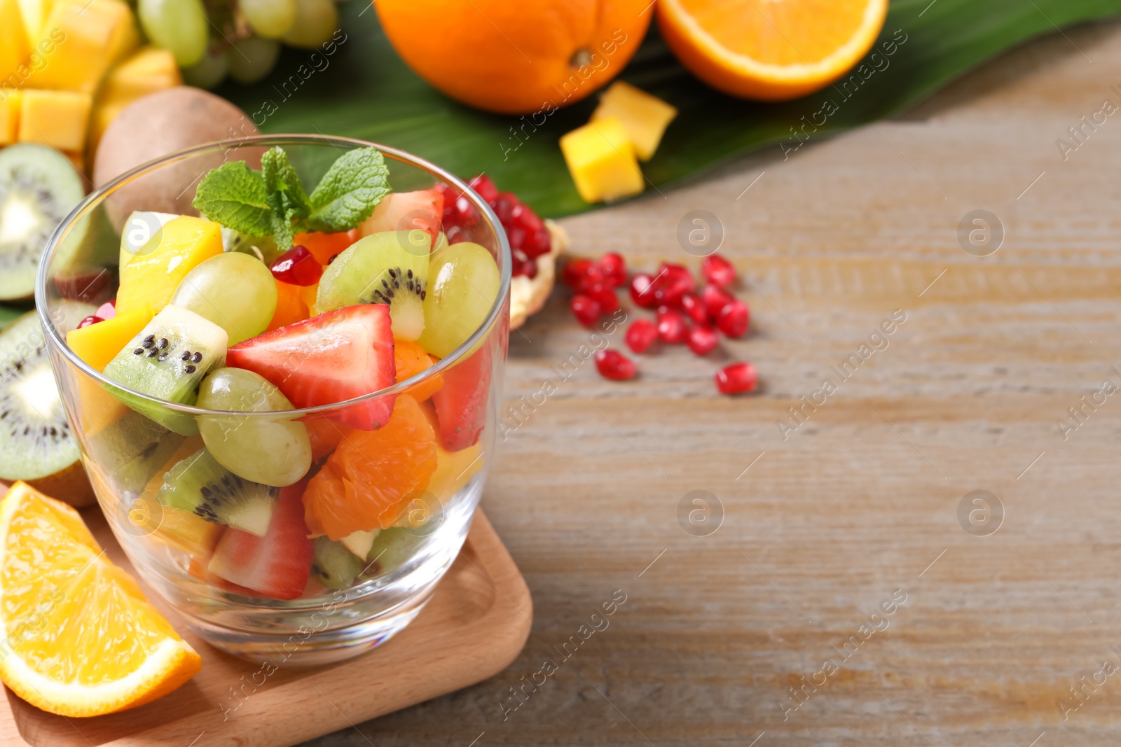 Photo of Delicious fresh fruit salad in dish on wooden table, space for text