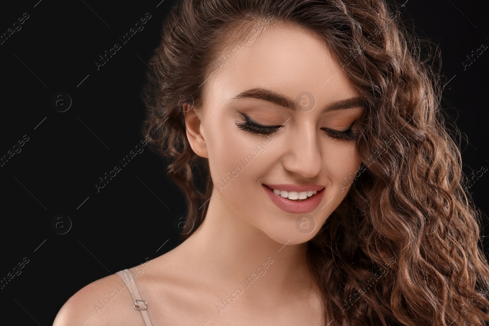 Photo of Beautiful young woman with long curly brown hair on black background, closeup