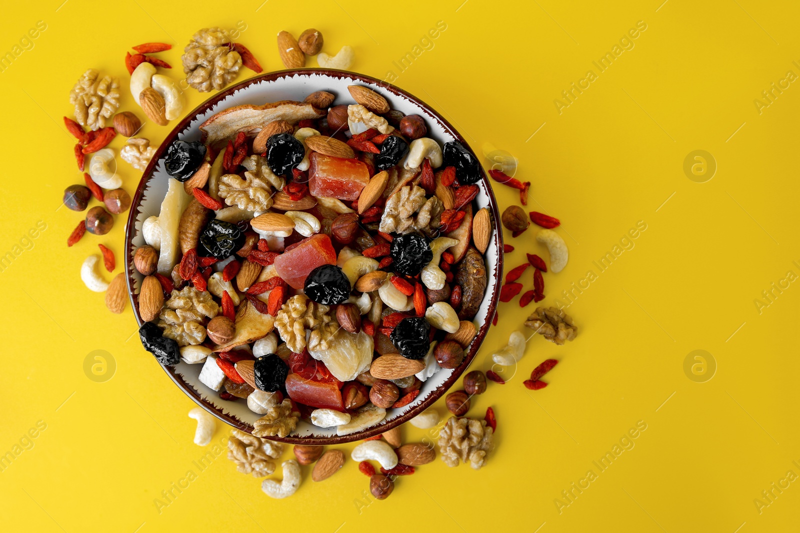 Photo of Bowl with mixed dried fruits and nuts on yellow background, flat lay. Space for text