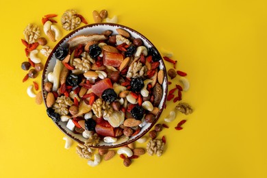 Bowl with mixed dried fruits and nuts on yellow background, flat lay. Space for text