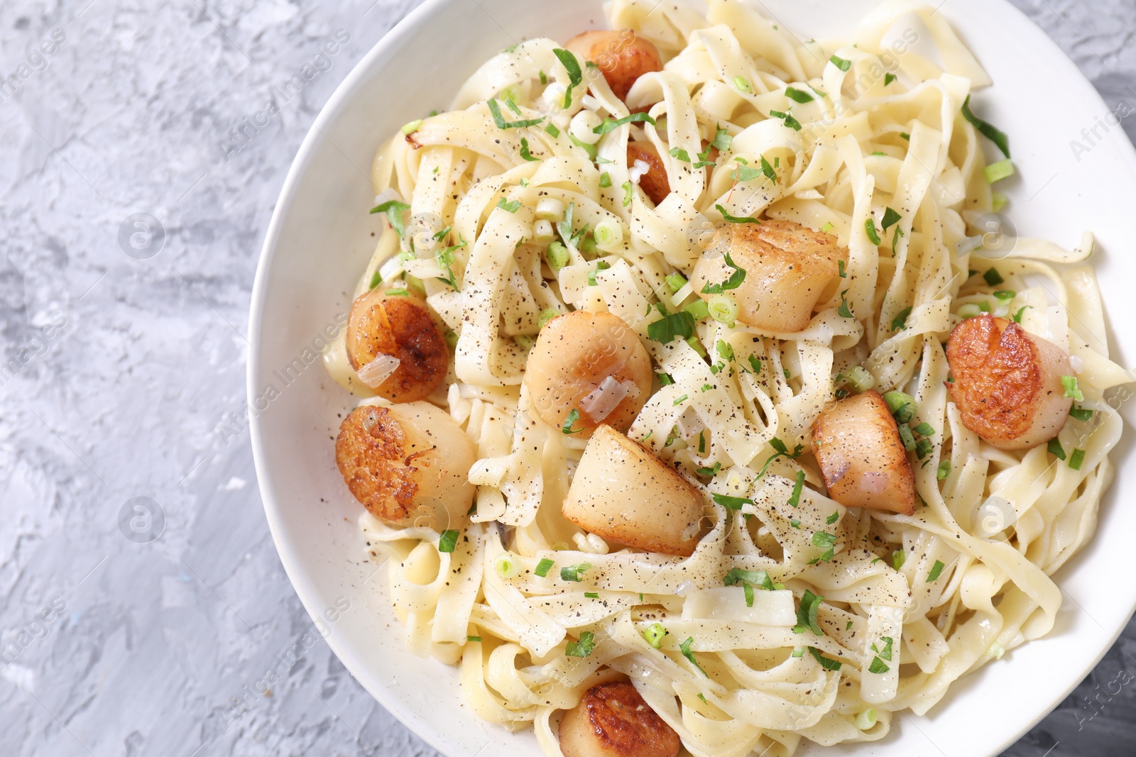 Photo of Delicious scallop pasta with spices in bowl on gray textured table, top view