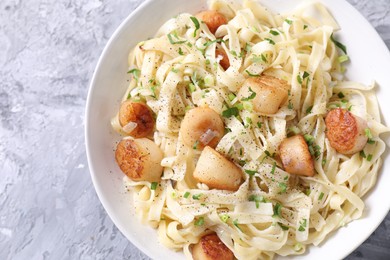 Delicious scallop pasta with spices in bowl on gray textured table, top view