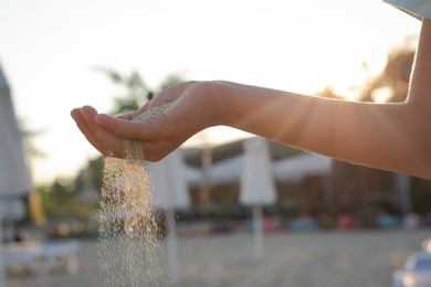 Photo of Girl pouring sand from hand on beach, closeup. Fleeting time concept