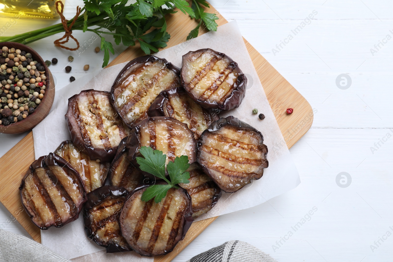 Photo of Delicious grilled eggplant slices with parsley and spices on white wooden table, flat lay