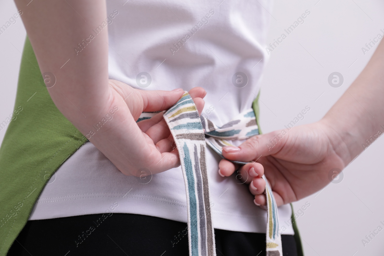 Photo of Woman putting on green apron against white background, closeup