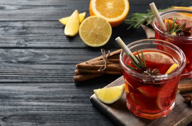 Photo of Aromatic punch drink and ingredients on black wooden table. Space for text