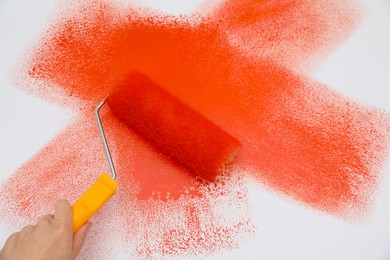Photo of Man applying orange paint with roller brush on white background, closeup