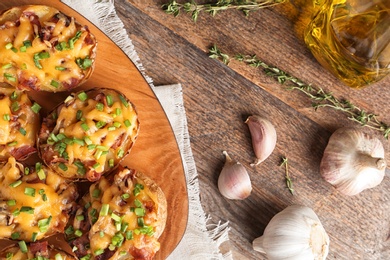 Flat lay composition with board of baked potatoes, garlic and oil on wooden background