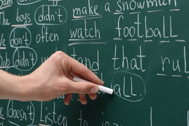 Photo of English teacher writing with chalk on green chalkboard, closeup